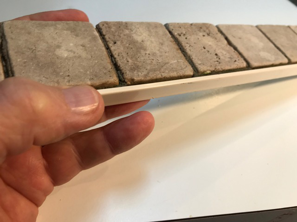 Hand holding a section of “paved” sidewalks for a garden railway