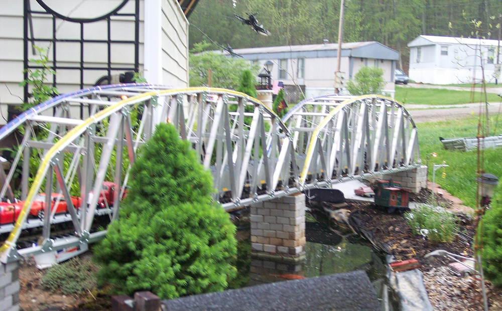 Silver bridge with conifer tree on garden railway