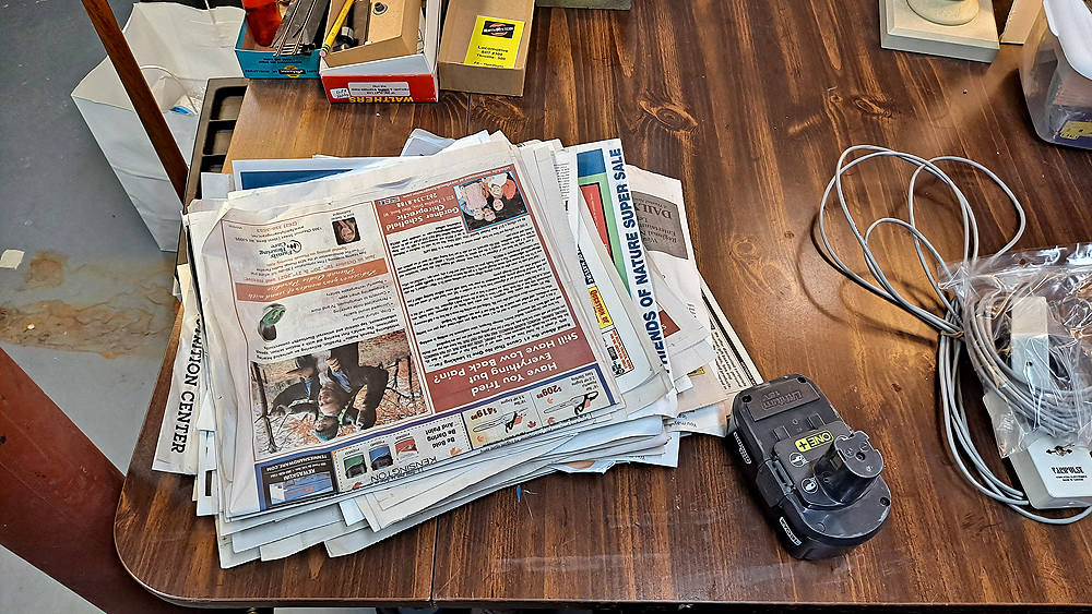 Newspapers are stacked on an old kitchen table in a basement.