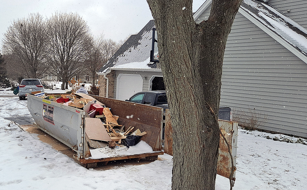 A gray construction Dumpster sits on a driveway on a snowy day.