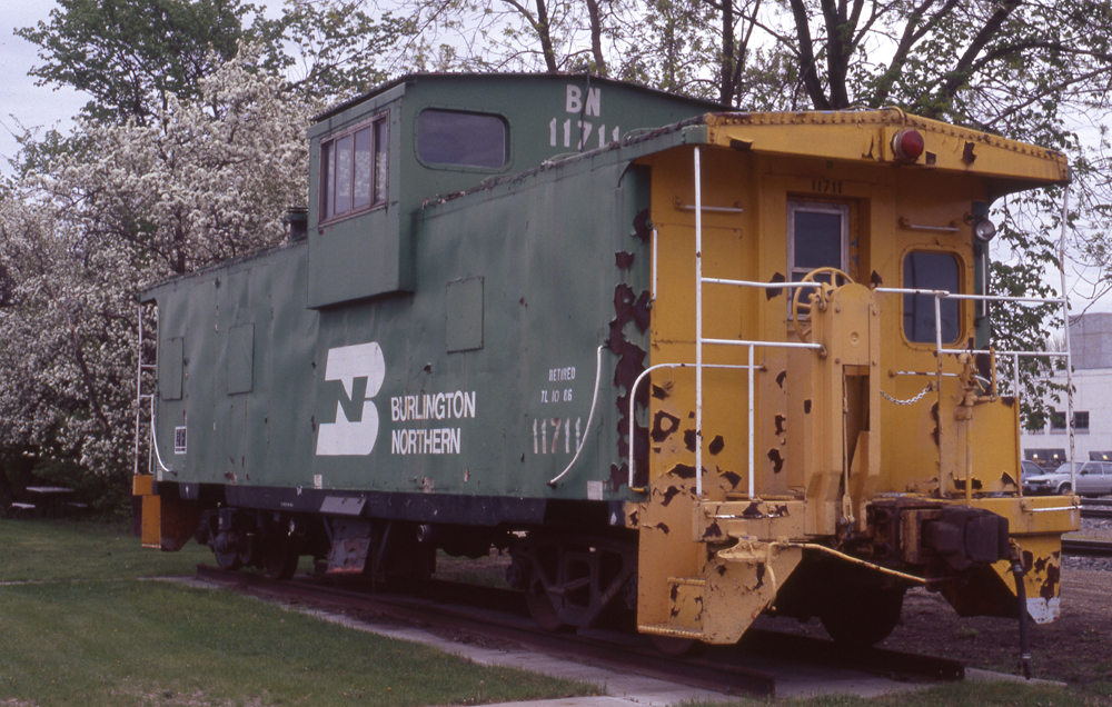 Green and yellow caboose on display in a park.