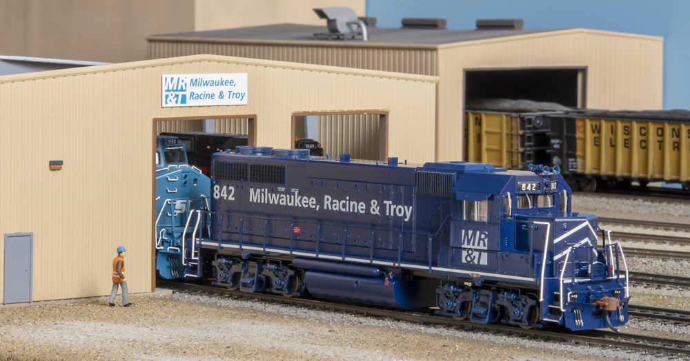Photo of dark blue diesel locomotive in front of building.