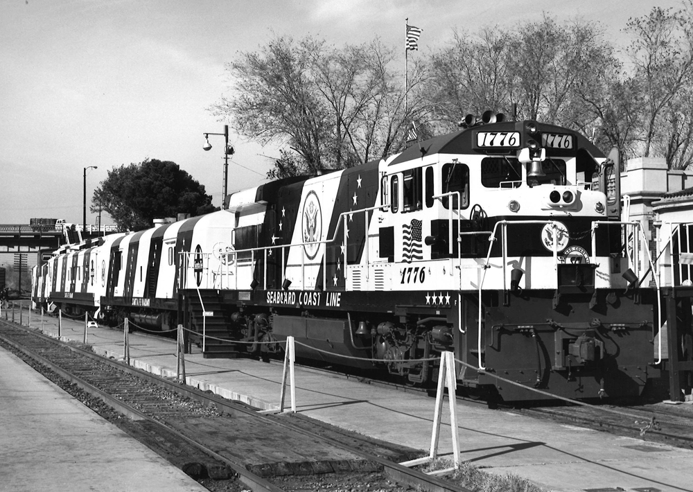 Black-and-white photo of locomotive, two baggage cars, and caboose painted in American Revolution Bicentennial colors. 