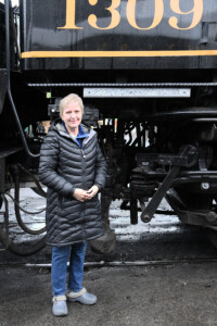 Lady standing next to cab of steam locomotive