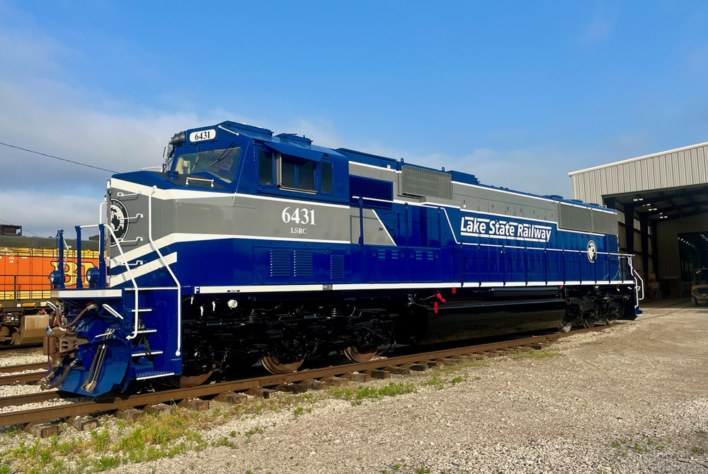 Freshly painted blue and grey locomotive in a rail yard.