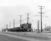 Baldwin locomotive with trolley pole extended pulling freight train.