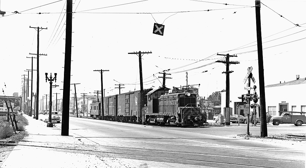 EMD locomotive with trolley pole extended pulling a freight train.