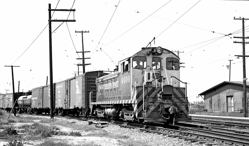 EMD locomotive with trolley pole extended pulling freight train through switches.