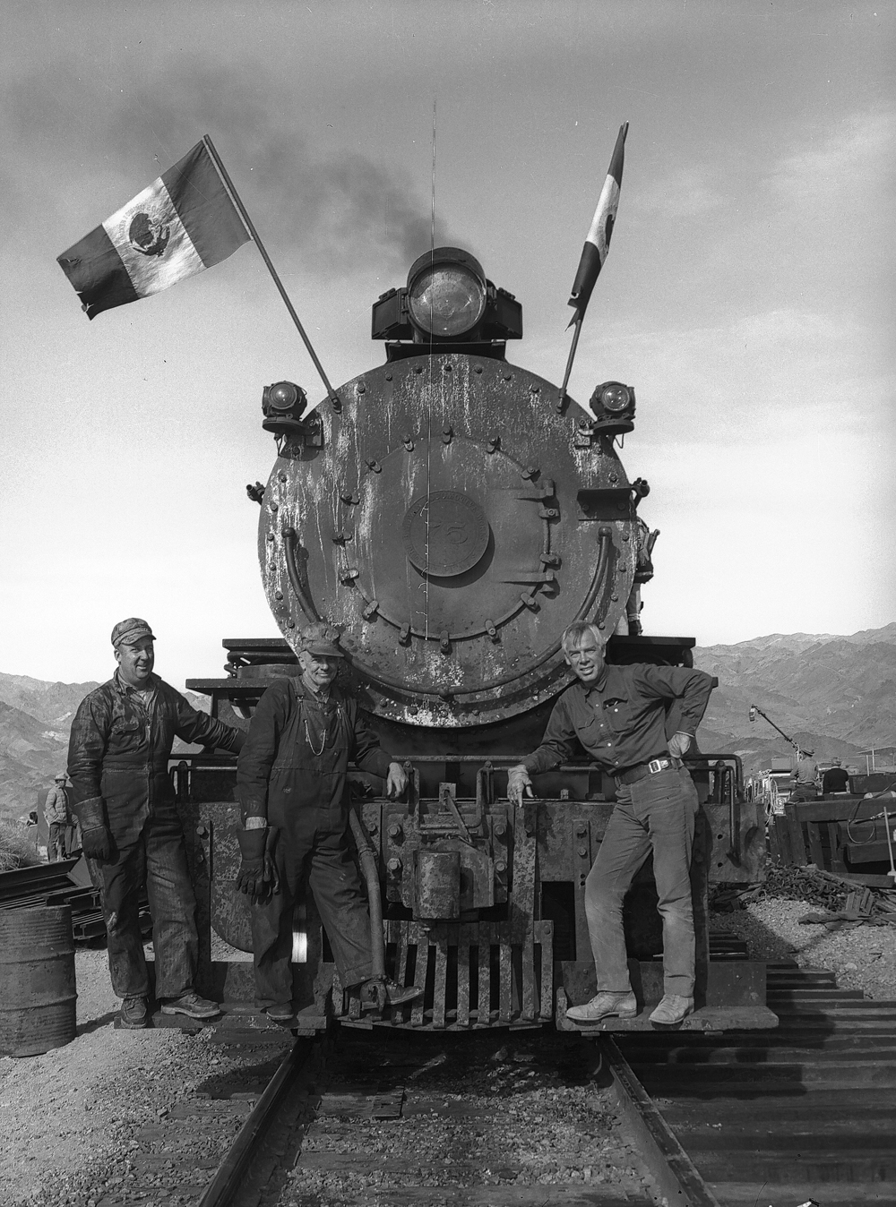 Men standing on the pilot of a steam locomotive.
