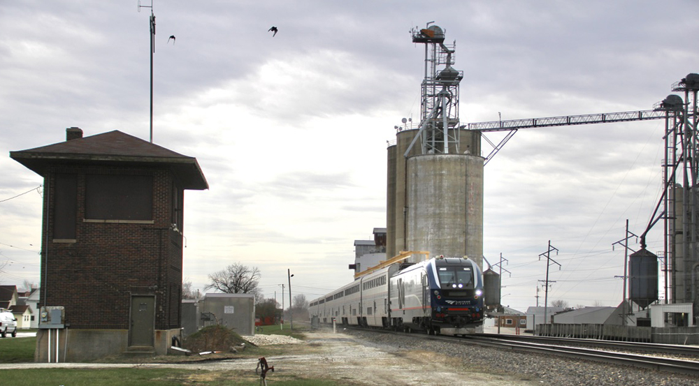 Passenger train passes grain elevator and closed interlocking tower