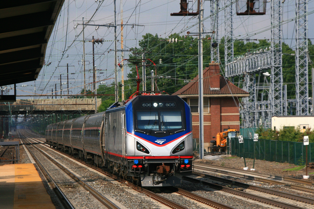 Train with electric lcomotive passes interlocking tower near station