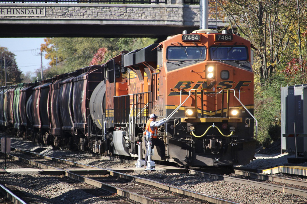 Man climbing on front steps of orange locomotive