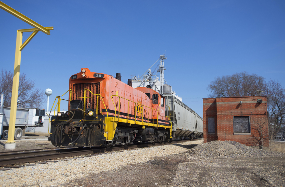 Orange locomotive passes brick building