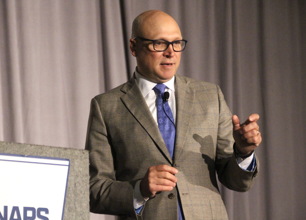 Man in brown suit gesturing while speaking