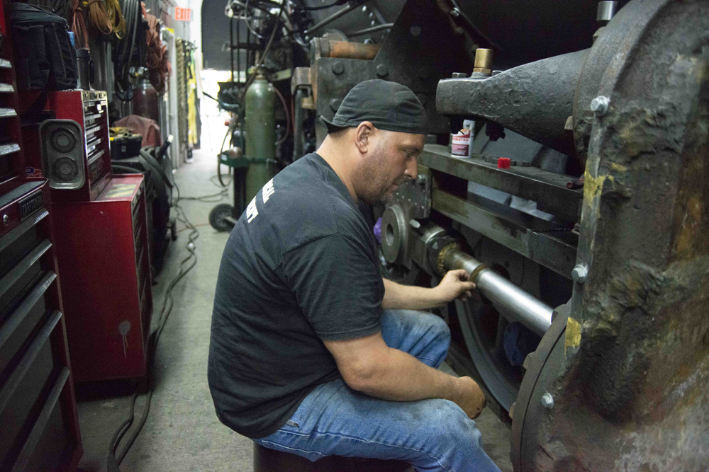 Man inspecting portion of steam locomotive