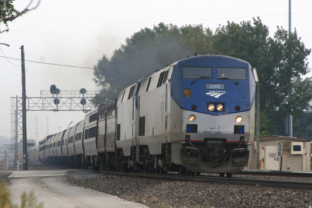 Long passenger train passes under signal bridge