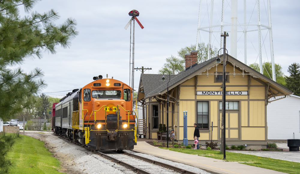 Orange locomotive on train next to yello wooden depot