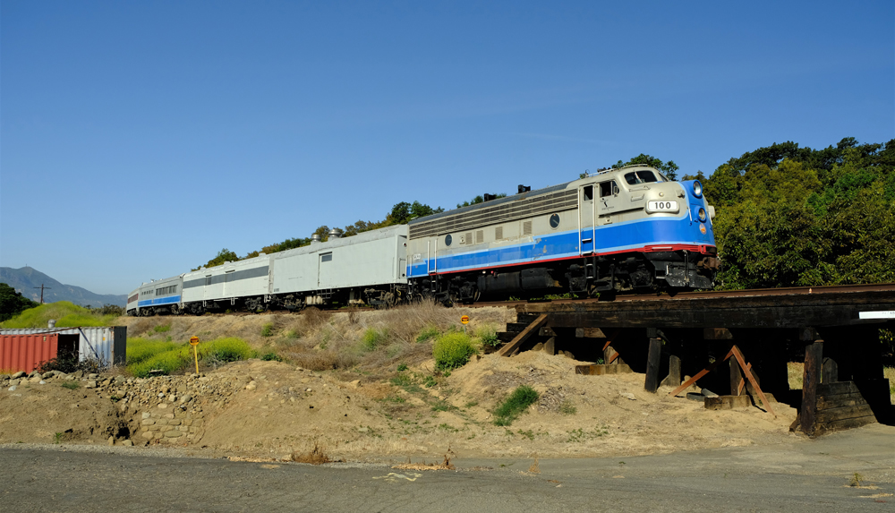 Blue and silver F unit with passenger cars crosses wooden bridge