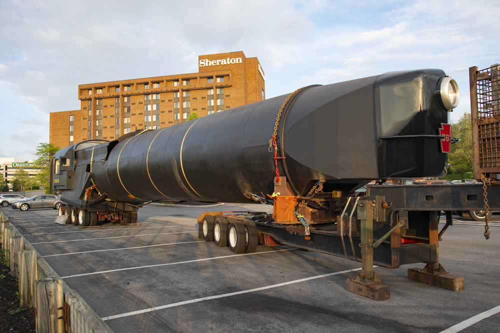 Long black bolier and related parts of steam locomotive under construction, mounted on wheels for highway movement