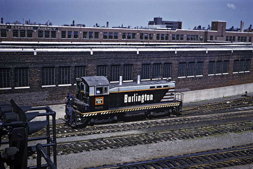 Black and gray end-cab locomotive by brick building
