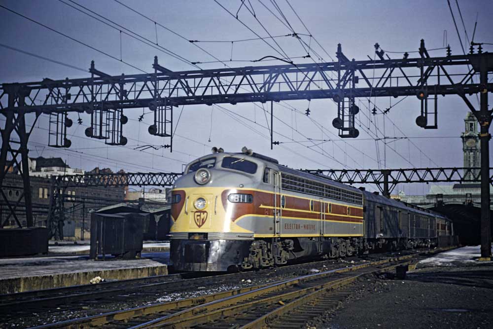 Streamlined gray, yellow, and maroon diesel locomotive under wires