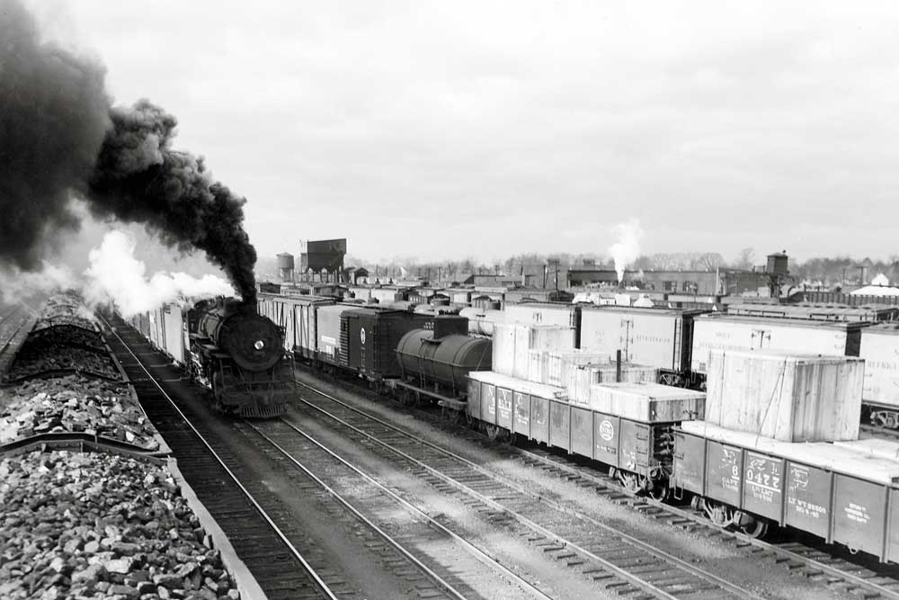 Smoking steam locomotive with train in freight yard