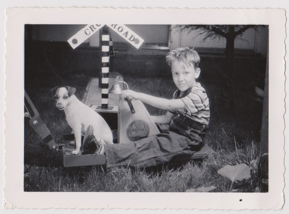 Black-and-white photo of child riding hand car with dog nearby