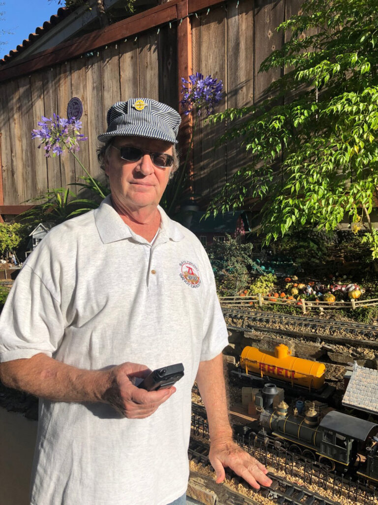 Man holding remote in hand, next to a garden railway
