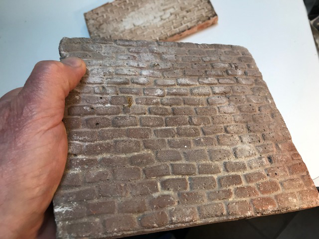 Hand holding a piece of concrete that looks like worn bricks