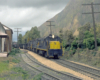 A blue C&O diesel with a yellow nose leads an ore train through an Appalachian landscape