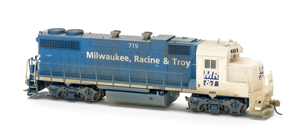 Photo of blue-and-white four-axle road locomotive on white background.