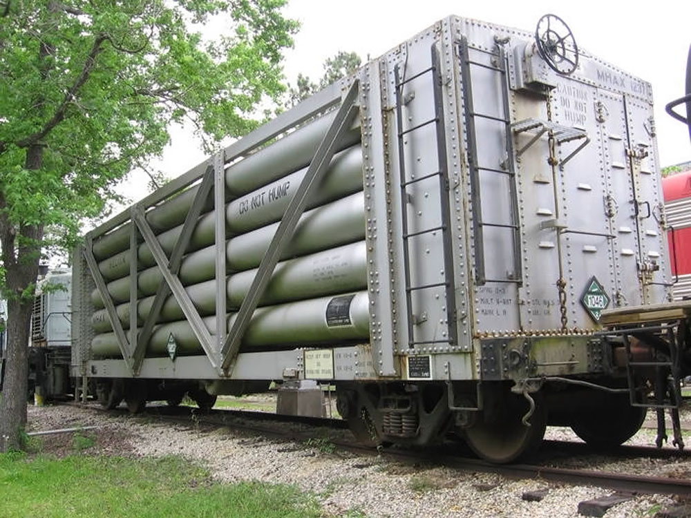 A silver rail car with doors on the end and a middle made up of narrow horizontal cylinders is seen in three-quarters view