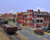 A steam engine switches a gondola of baled scrap metal next to an old-fashioned downtown scene