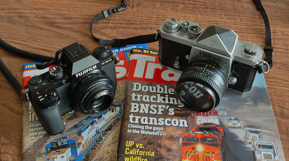 Digital and film cameras placed on copies of Trains magazine.