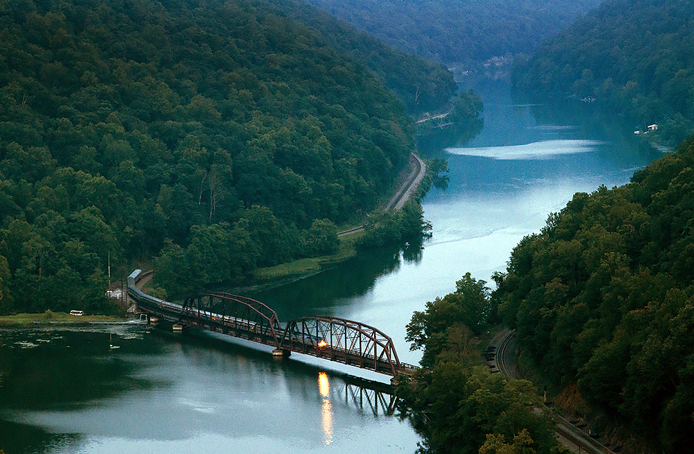 Train crossing a bridge over a river in dim twilight.