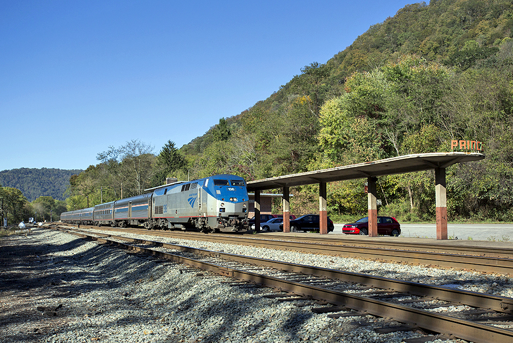 Passenger train at a station platform in a mountainous area under clear skies in summer.