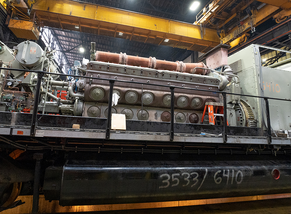 Locomotive prime movers: A multicolored prime mover in a locomotive body in a cavernous shop without the locomotive's exterior body work or shell.