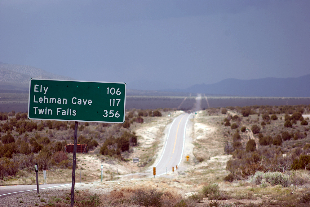 Road sign showing distances to places hundreds of miles away in an arid scene.