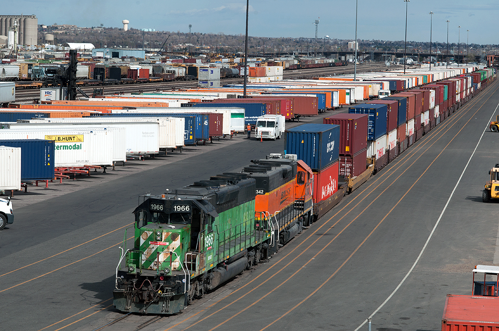 A green locomotive leads a freight train in a rail yard.