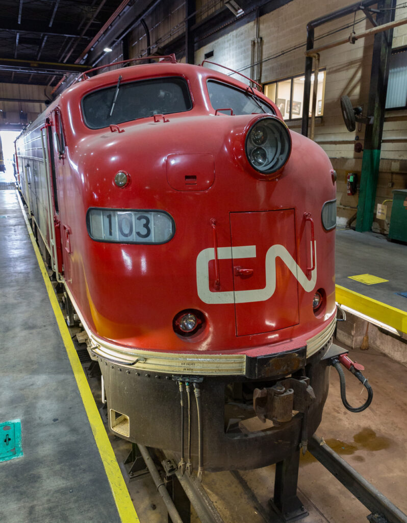 Locomotives with two diesel engines: A red cab unit locomotive in a shop building.