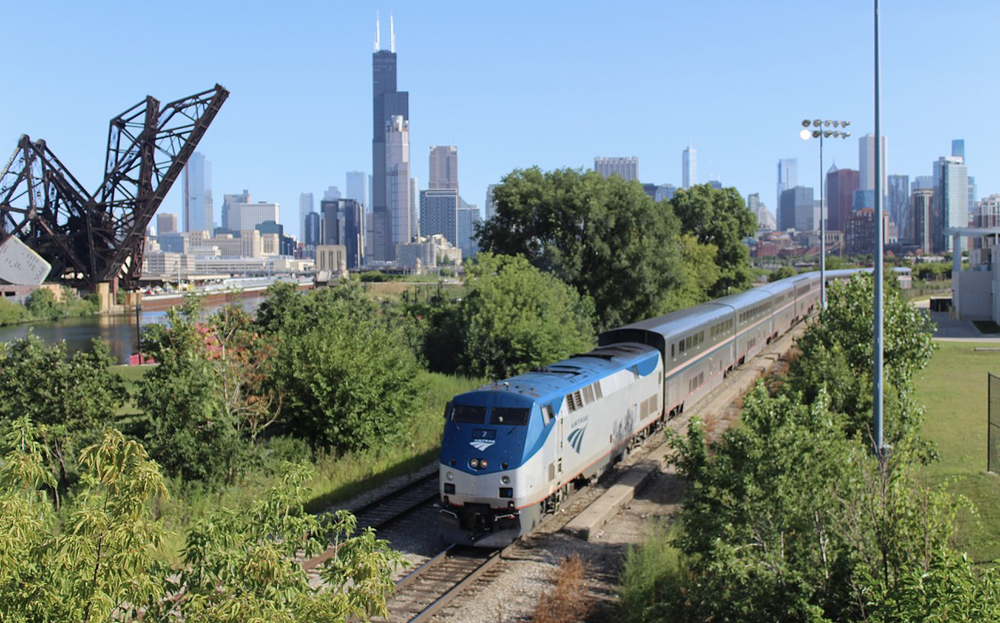 Passenger train runs on single track with Chicago skyline in the background