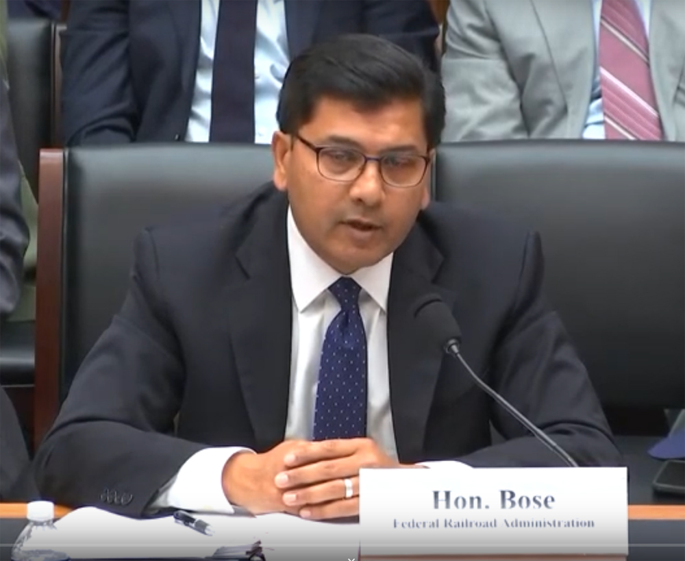 Man speaking into microphone while seated at table