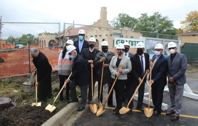 People in hardhats with shovels in front of train station