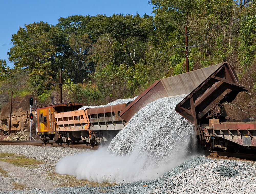 Side-dump gondola unloads rock next to rail line