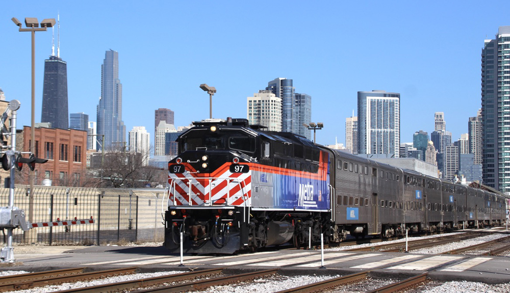Train with stainless steel passenger cars and Chicago skyline in the background