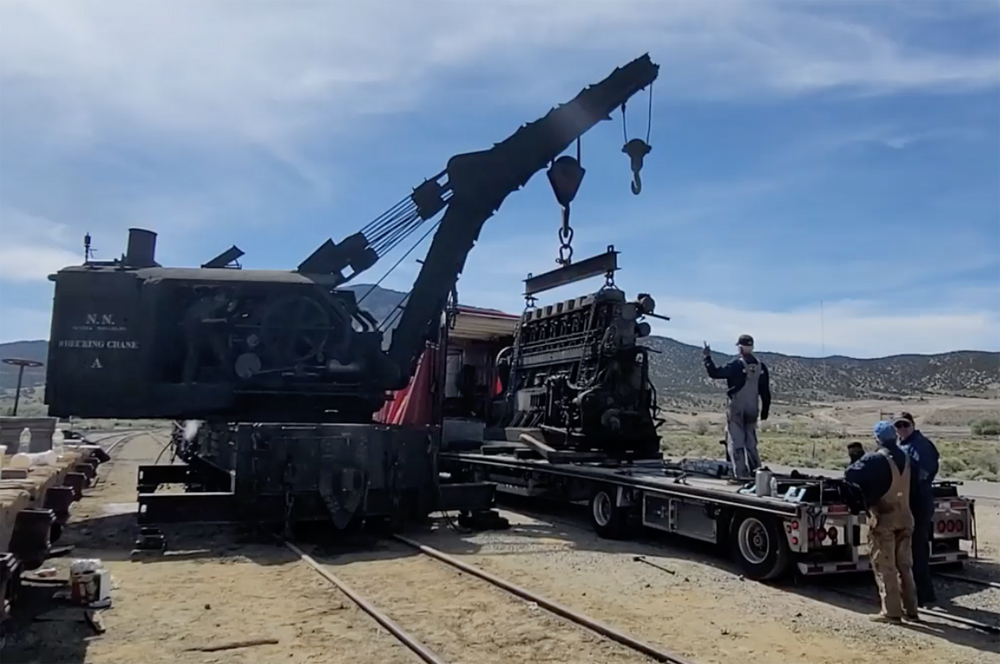 Black crane lifting diesel engine off trailer