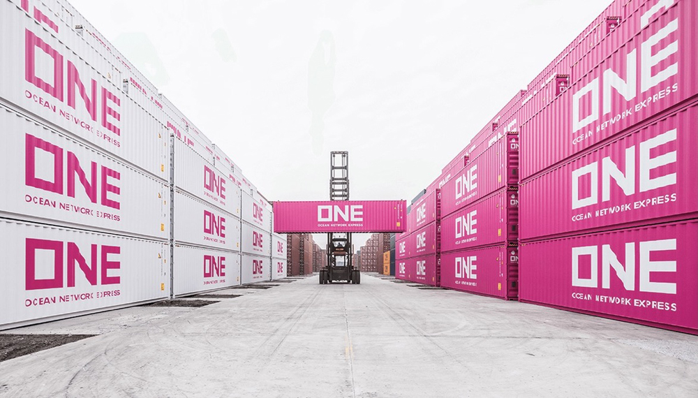 Pink and white intermodal containers, with tractor lifting one box in center of photo