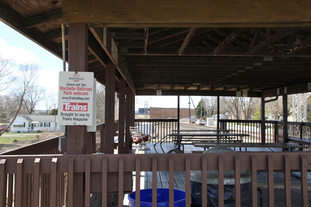 Covered platform with tables and chairs, with railroad tracks visible in background