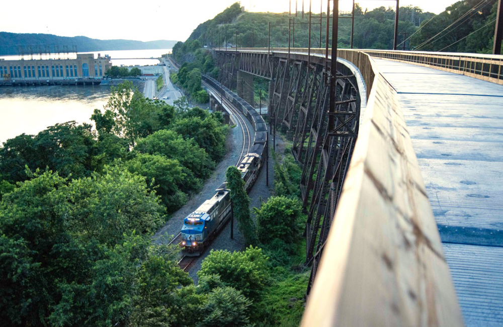 As seen from deck of high bridge, coal train rounds curve on tracks below