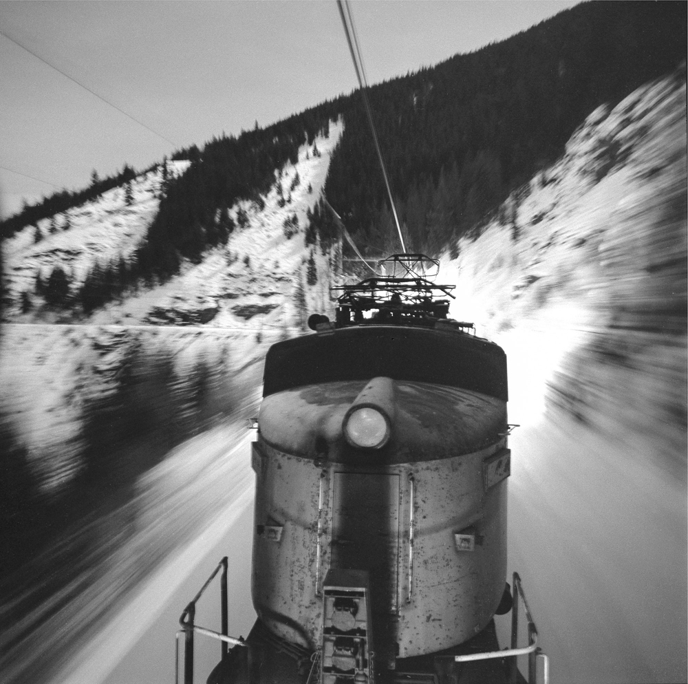 Black-and-white photo of electric locomotives in mountains, taken from on board train